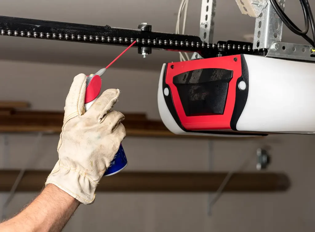 Worker using lubricant to perform maintenance on garage door opener components