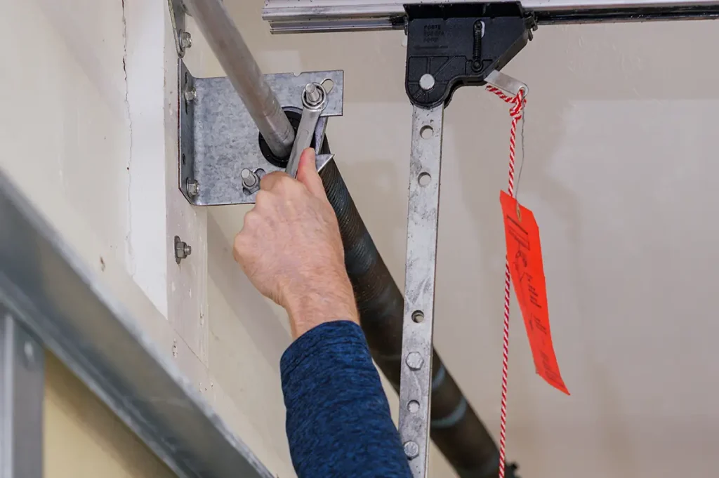 A person's hand repairing a garage door spring bolts