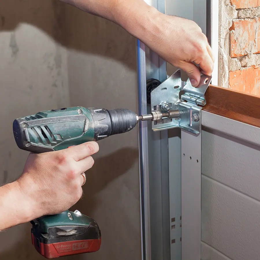 Worker using electric screwdriver to install garage door components