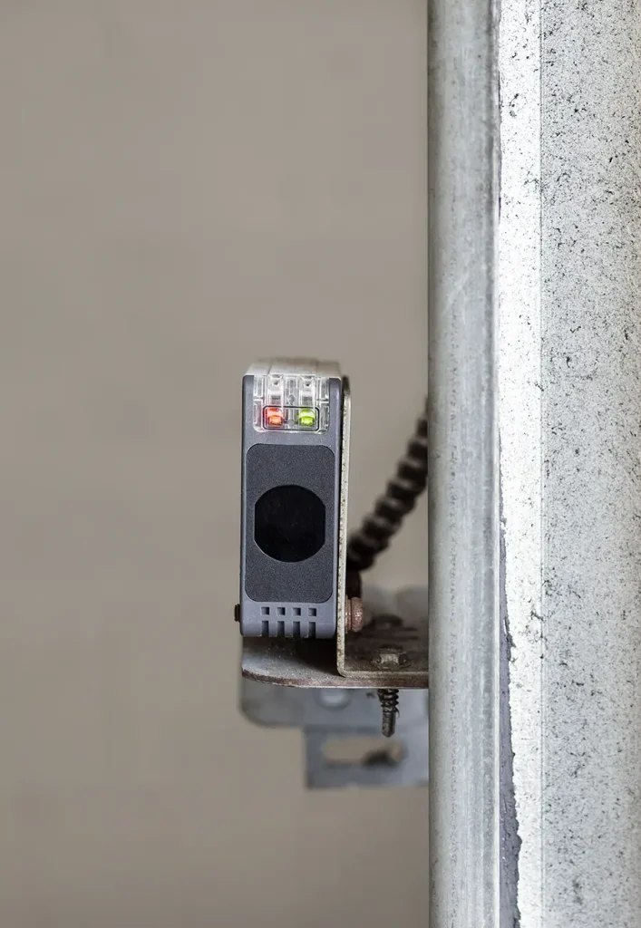 Garage gate sensor mounted on wall. Close up of photoelectric sensor with connected to overhead sectional door.