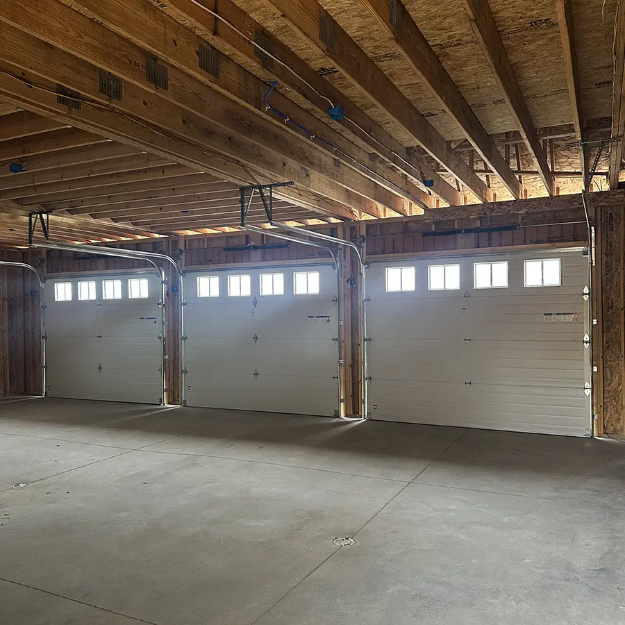 Garage with exposed roof beams and light coming in through three garage doors